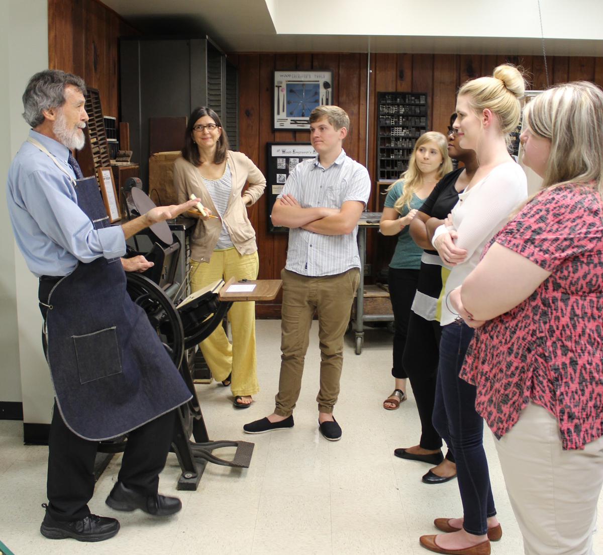 A man wearing an apron gestures as he speaks to a small group of students standing in a circle.